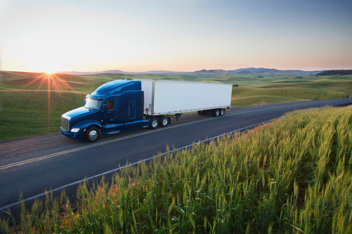 Big blue truck on a remote highway used to illustrate that GEICO provides insurance coverage for well-known brands like Freightliner and Kenworth.