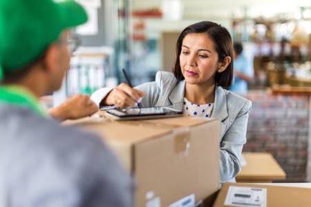 A small business owner signing for a package that is being delivered by a courier service. The image is used to showcase the importance of general liability insurance to safeguard businesses from claims that may result from normal business operations.
