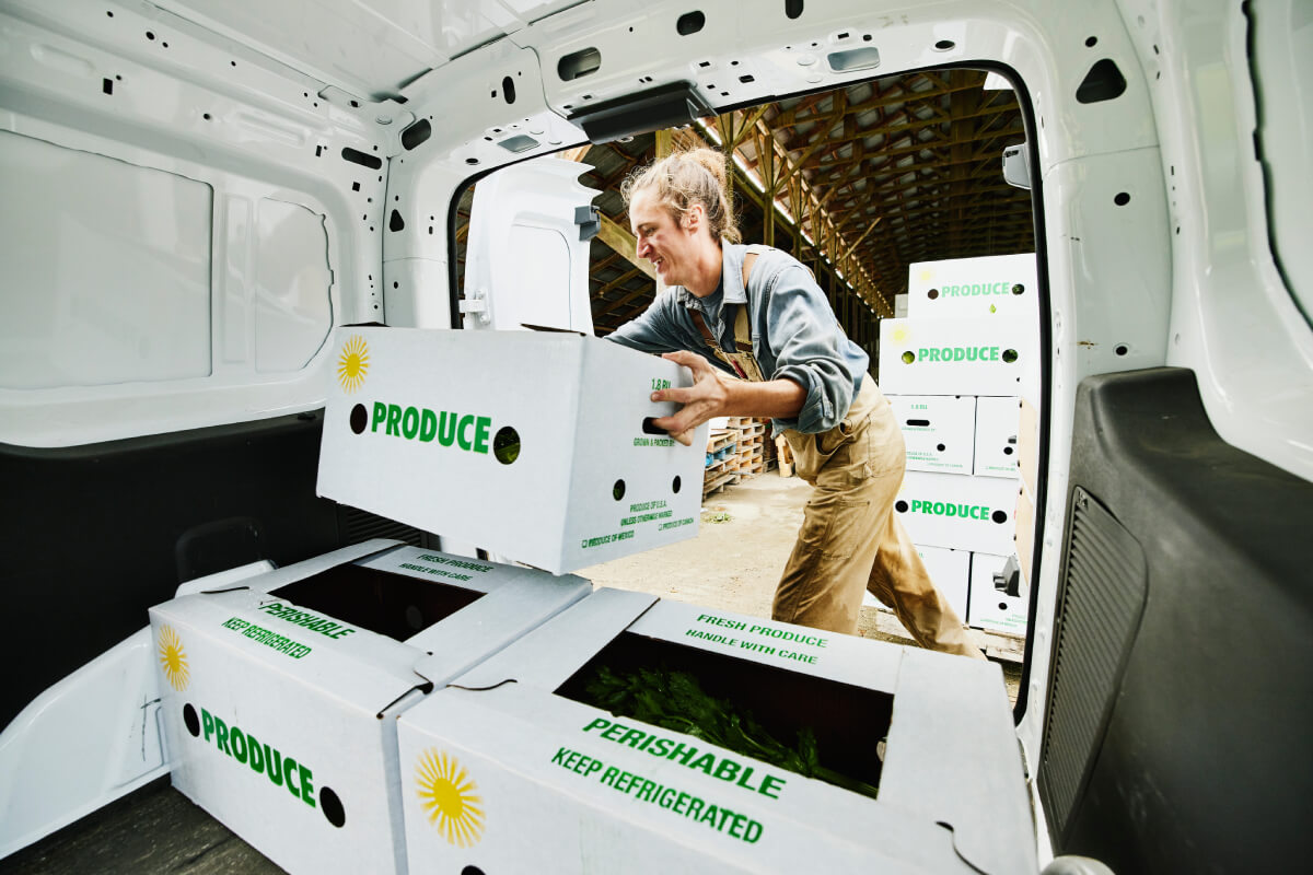 A smiling young farmer loading fresh produce to the back of his truck, used to depict the importance of truck insurance for private carriers, like farmers, hauling goods for their own company.